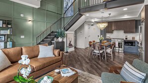 A spacious living area with a brown leather sofa, a dining table with chairs, a staircase, and a kitchen with modern appliances. - AlpenPeak Hydeaway at Ascent (Canmore)