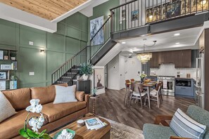 Uma sala de estar ampla com um sofá de couro marrom, uma mesa de jantar com cadeiras, uma escada e uma cozinha com eletrodomésticos modernos.