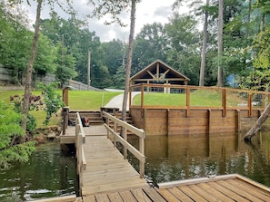 A wooden dock leading to a small wooden structure with a sloped roof, surrounded by a grassy area and trees. - 3-bedroom riverfront house on Angelina River (Jasper)