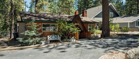 A cabin with a front porch, a bench, and a driveway leading to the entrance.