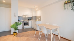 A modern kitchen with white cabinets, a dining table with chairs, and a potted plant. - Amazing Apartment in Antwerp (Antwerp)