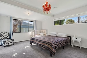 Ein Schlafzimmer mit Bett, Nachttisch, Sessel, Fenster und einer Chandelier.