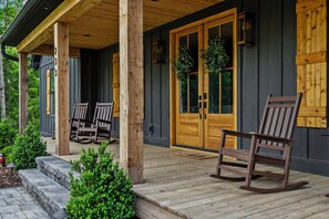 A wooden porch with two rocking chairs, a wooden bench, and a door with glass panels.