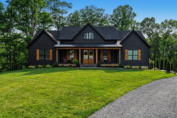A two-story house with a dark exterior, a front porch, and a well-maintained lawn.