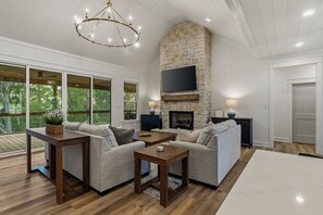 A modern living room with a stone fireplace, large windows, and a flat-screen TV.