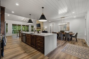 A modern kitchen with a large island, dark wooden cabinets, and pendant lighting.