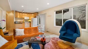 Ein modernes Wohnzimmer mit einem Glastisch, einem orangefarbenen Sofa und einem blauen Sessel.