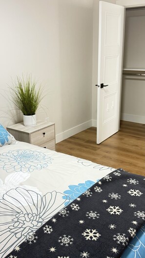 A bedroom with a bed, a nightstand with a plant, a white door, and a wooden floor. - SERENE COASTAL ESCAPE (Surrey)