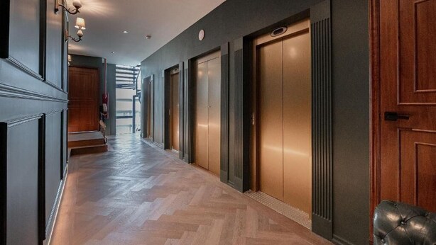 A hallway with wooden flooring, a leather bench, and a set of elevators. - The Tub Suite (Mexico City)