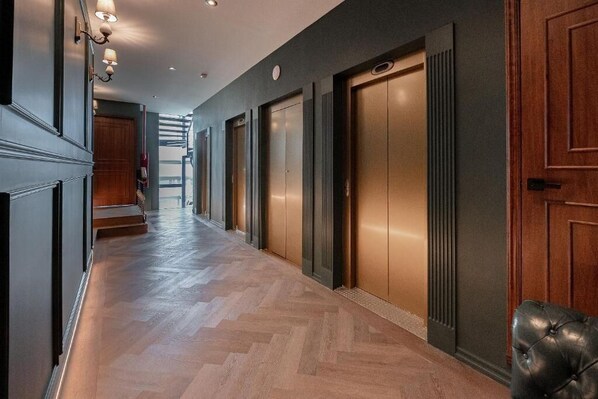 A hallway with wooden flooring, a leather bench, and a set of elevators. - The Tub Suite (Mexico City)
