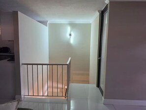 Eine Treppe führt zu einer Zwischenebene mit einem weißen Geländer, einer Wandleuchte und einer Tür rechts.