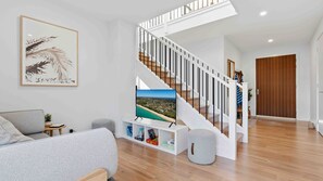 Un salon moderne avec un escalier, un téléviseur à écran plat, une œuvre d’art encadrée et un canapé gris.