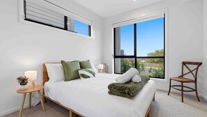 Un dormitorio con una cama grande, una silla, una mesita de noche y una ventana con vistas.