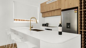 Eine moderne Küche mit weißer Arbeitsplatte, goldenem Wasserhahn, einer Weinflasche und einem Weinkühler.