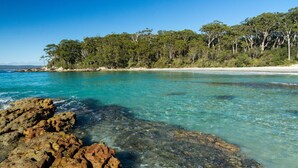 A coastal landscape with clear turquoise waters, rocky shorelines, and a dense forested area. - Vinny Ocean View by Experience Jervis Bay (Vincentia)