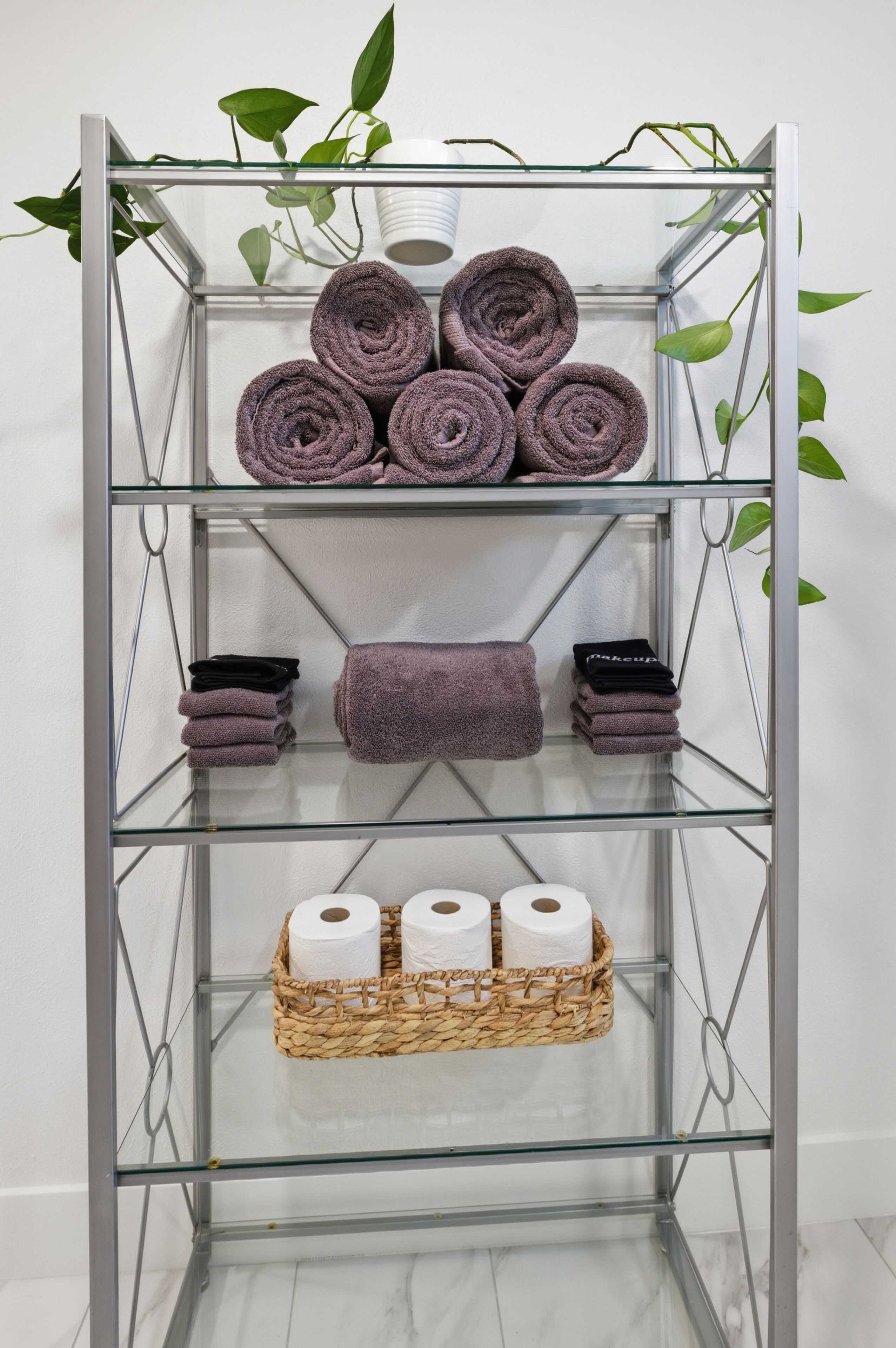 A metal shelf unit with rolled towels, a basket of toilet paper, and a potted plant.