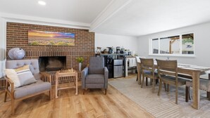 Een woonkamer met een haard van baksteen, een bank, een salontafel en een eethoek met stoelen en een tafel.