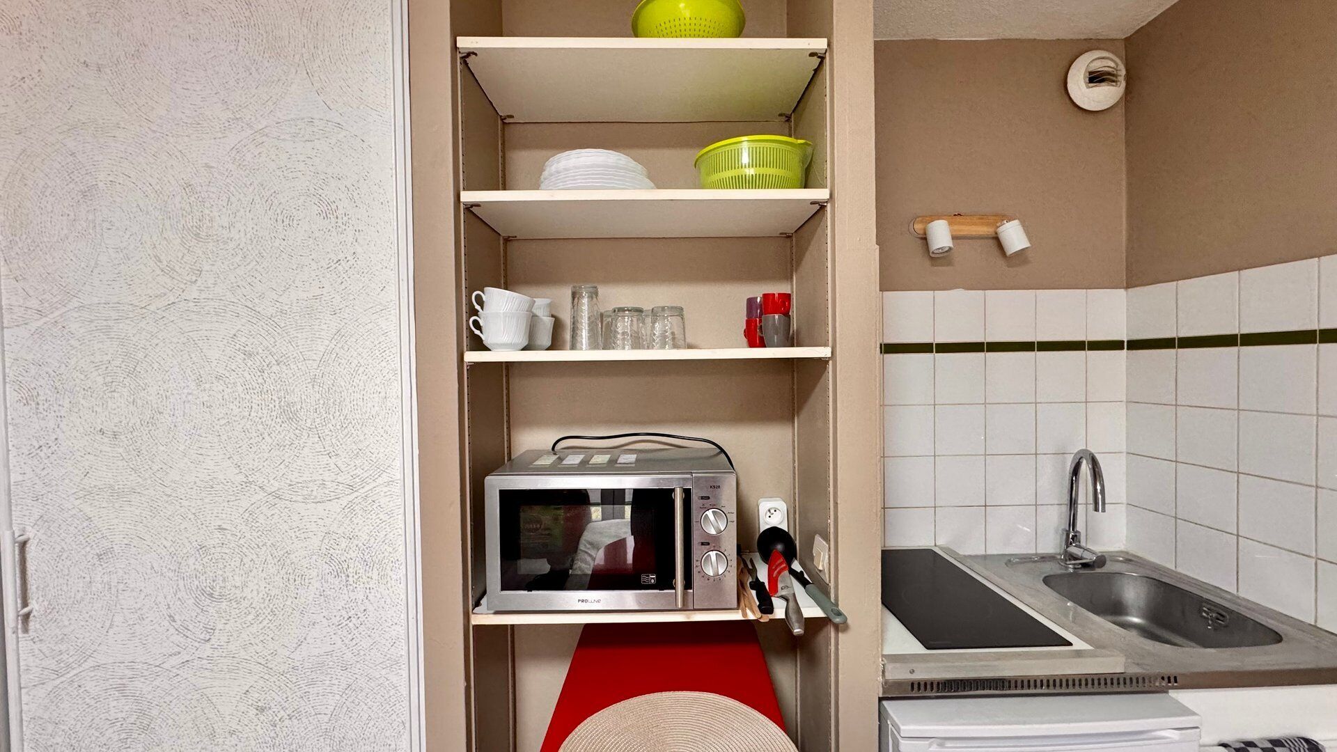 Une cuisine compacte équipée d’un four à micro-ondes, d’un évier et d’étag ères contenant des ustensiles de cuisine.