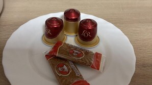 A white plate with four red and gold coffee cups and two brown coffee packets on a wooden surface.