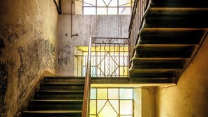 Eine Treppe mit Holzgeländer, einem Schachbrettfußboden und einem Fenster mit geometrischem Muster.