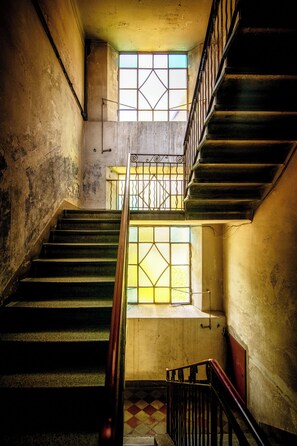 Eine Treppe mit Holzgeländer, einem Schachbrettfußboden und einem Fenster mit geometrischem Muster.