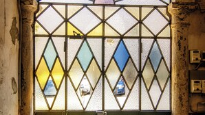 Eine Buntglas-Tür mit geometrischen Mustern, ein Metallgitter und ein Steinunterbau.