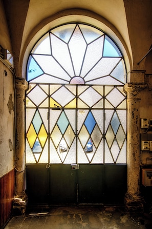 Eine Buntglas-Tür mit geometrischen Mustern, ein Metallgitter und ein Steinunterbau.