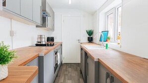 A modern kitchen with wooden countertops, stainless steel appliances, and a window with a view. - Armstrong St - Cosy 3 Bedroom Home (Workington)