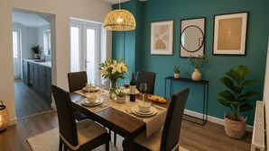 A dining area with a table set for four, chairs, a hanging light fixture, and wall-mounted artwork. - Armstrong St - Cosy 3 Bedroom Home (Workington)