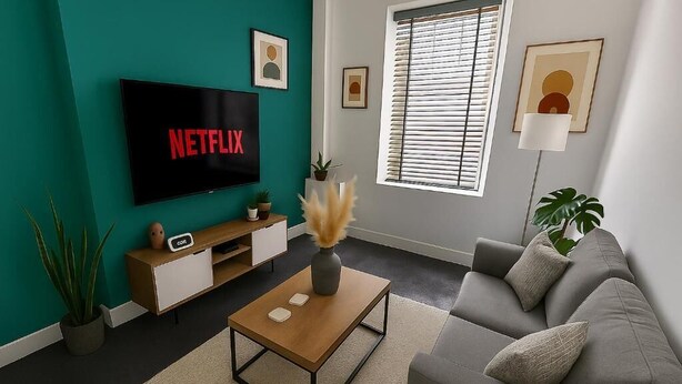 A living room with a TV displaying 'NETFLIX,' a sofa, a coffee table, and a window with blinds. - Armstrong St - Cosy 3 Bedroom Home (Workington)