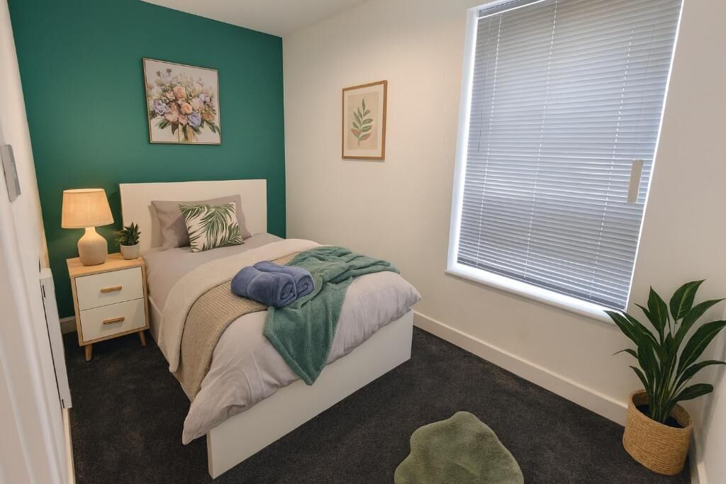 A bedroom with a bed, bedside table, lamp, and a window with blinds.