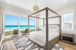 Un lit à baldaquin avec vue sur la plage, un balcon avec une chaise et une table de chevet avec une lampe.