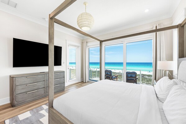 Un dormitorio con una cama grande, televisión, cómoda y balcón con vista al océano.