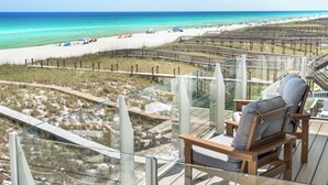 A deck with a glass railing overlooking a beach with a sandy shore and a clear blue ocean. - 💎 Share My Lowecation! Brand New Lux 6BR Beachfront! Pool, Pets, Sleeps 16 (Navarre Beach)