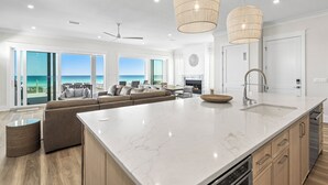 A spacious living area with a large island, a kitchen with modern appliances, and a view of the ocean. - 💎 Share My Lowecation! Brand New Lux 6BR Beachfront! Pool, Pets, Sleeps 16 (Navarre Beach)