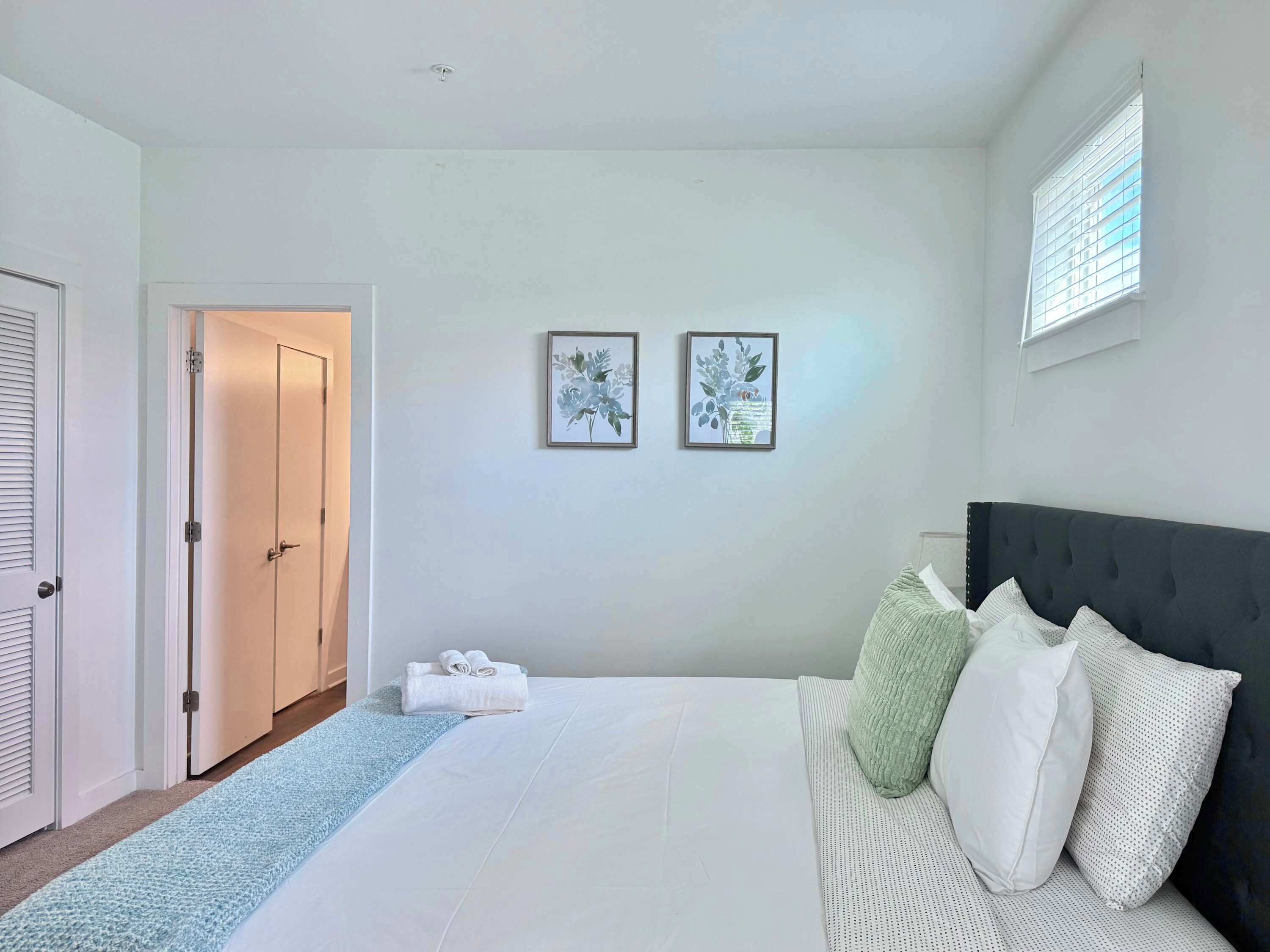 A bedroom with a bed, a door, a window, and two framed pictures on the wall.