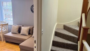Ein Wohnzimmer mit einer Couch, gemusterten Kissen, einer Uhr an der Wand und einer Treppe mit Teppichstufen.