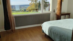 A bedroom with a bed, a chair, a table, a radiator, and a window with a view of a landscape. - Normandy: Chic & Authentic (Beaumont-le-Roger)
