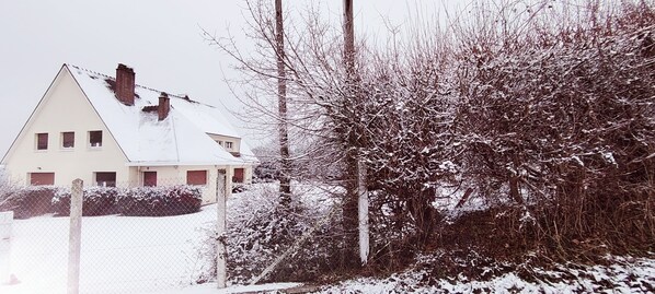 A house with a sloped roof, a fenced yard, and snow-covered trees.