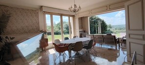 A dining area with a table and chairs, large windows, and a chandelier.