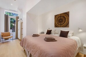 Un dormitori amb llit, almoines, una cadira, una obra d'art a la paret i una porta que dona a zona exterior.