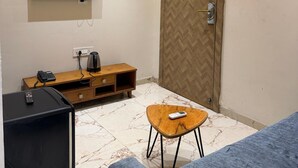 A room with a flat-screen TV mounted on the wall, a wooden entertainment unit, a sofa, a small wooden table, and a door with a herringbone pattern. - Vijaya's Homestay Indore (Indore)