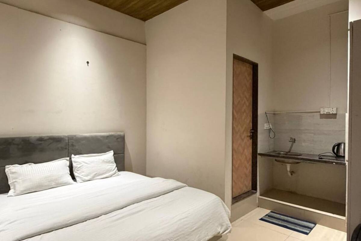 Un dormitorio con cama, ventilador de techo, techo de madera, baño con lavamanos y espejo, y suelo de baldosas.