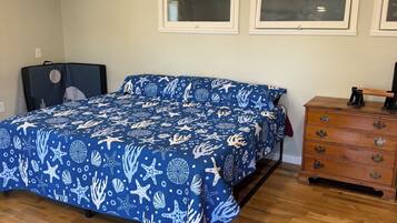 Un dormitorio con cama, cómoda, ventilador de techo y dos ventanas.