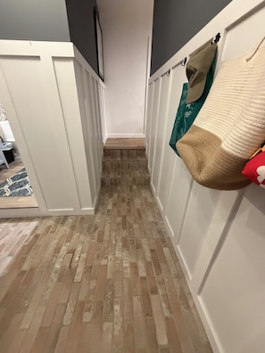 A narrow hallway with a wooden floor, white walls, and a door on the left.
