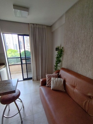 A modern living room with a brown leather sofa, a small table, and a potted plant. - Studio Urbano-flat confortável-localização nobre (Goiânia)