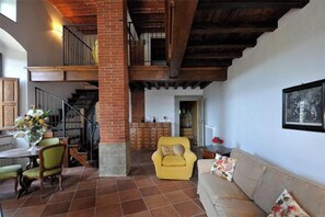 Ein geräumiger Wohnbereich mit Treppe, einem gelben Sessel, einer Couch und einem Esstisch mit Stühlen.