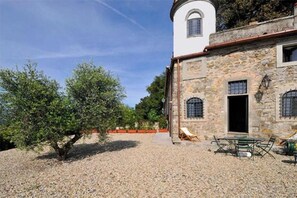Ein Steinhaus mit einem weißen Turm, Außenbestuhlung und einem Kieshof.