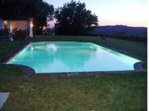 Ein rechteckiger Pool mit einer umlaufenden Rasenfläche und einem Haus im Hintergrund.