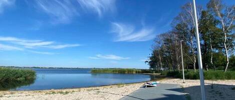 Ein klarer Himmel, ein ruhiger See, ein Sandstrand und ein Holzsteg mit einem Boot.